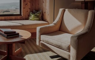 Beige sofa chair next to coffee table in a room with sun shining through.