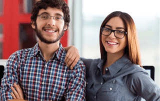 Two young adults wearing glasses smiling.