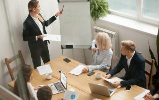Woman presenting to team in small conference room.