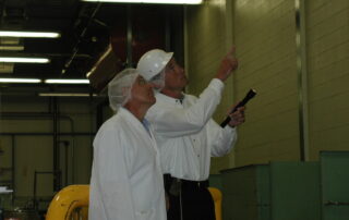 A lab worker speaks with a pest control specialist, who are both wearing white protective gear